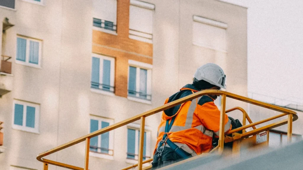 Worker in safety gear operating a lift near an apartment building