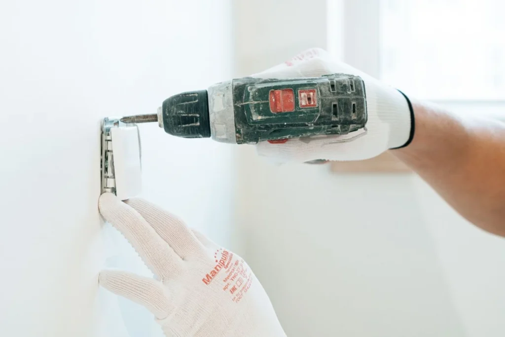 Gloved hands using a drill to install a power outlet