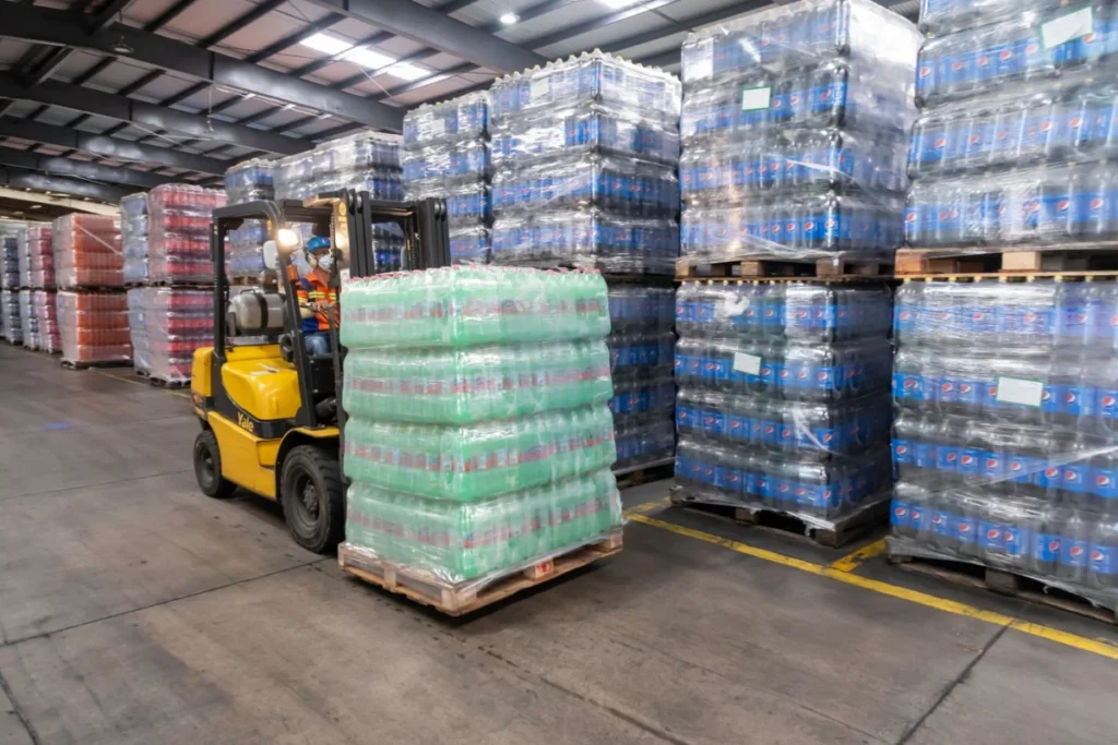 Forklift operator moving stacked pallets in a warehouse