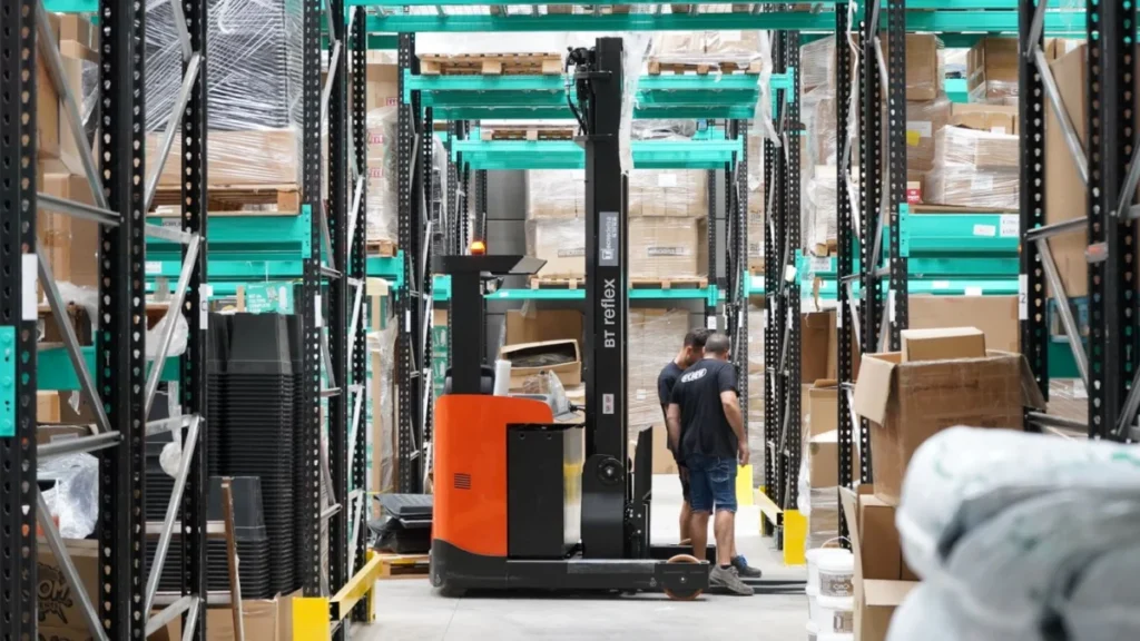 Warehouse workers and a forklift in the aisles