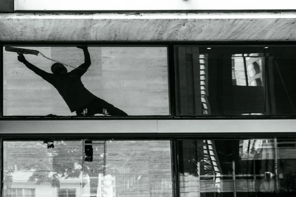 Silhouette of a window cleaner with squeegee on building glass, reflecting urban architecture