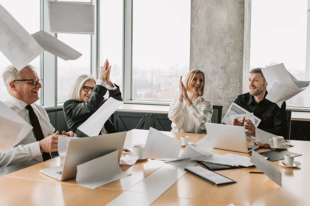 Group of happy coworkers celebrating a successful meeting, throwing papers and clapping in a modern office