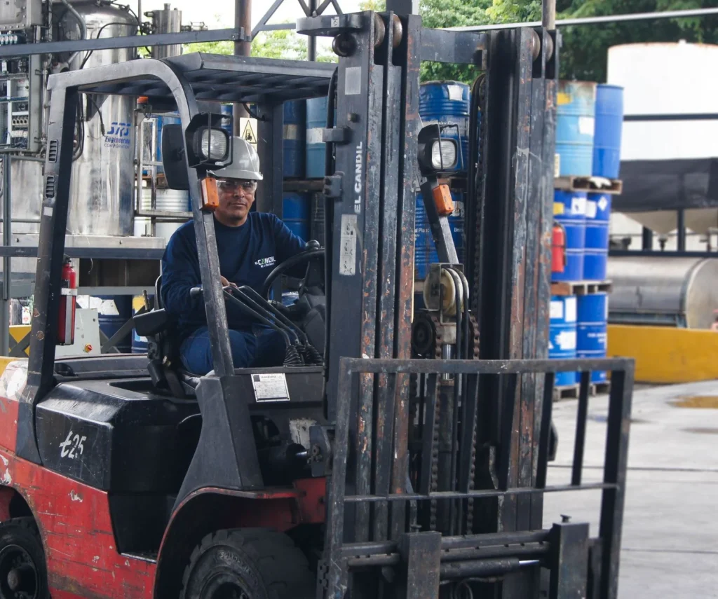 Warehouse scene with worker operating a forklift among blue barrels