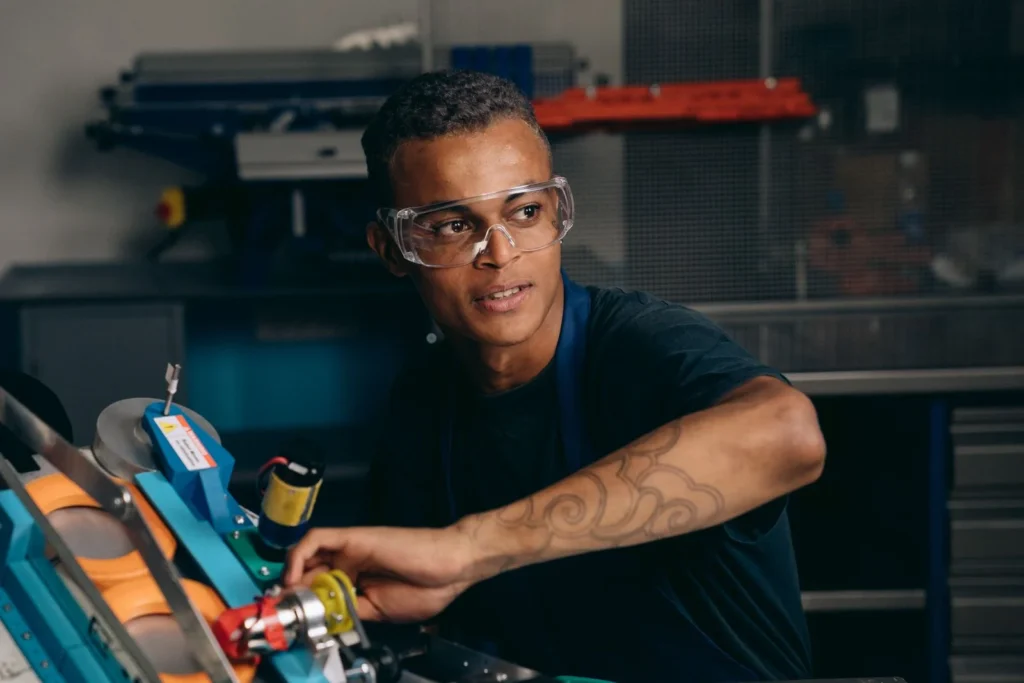 Young engineer working with machinery in a manufacturing setting, wearing safety glasses and focusing intently