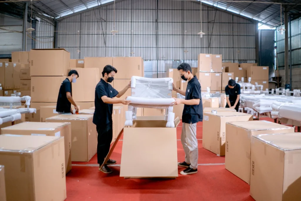 Men in a warehouse wearing masks, assembling and packing furniture into boxes with efficiency